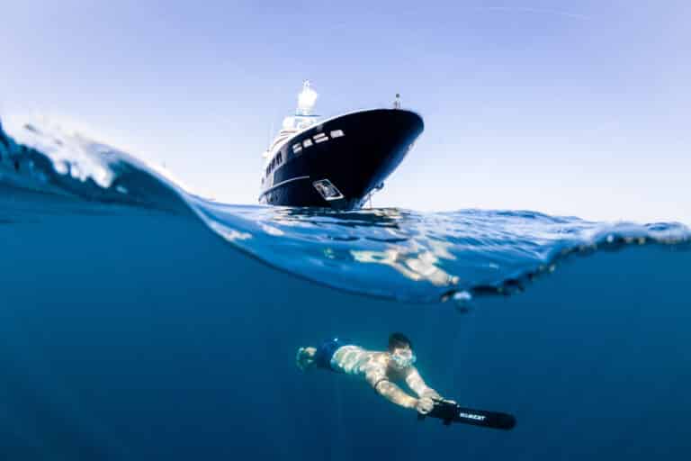 Swimmer underwater beside a yacht